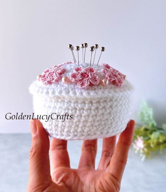 Sweet and elegant, this white crochet pincushion looks just like a tiny dessert. Decorated with tiny pink flower appliques and beads, it feels delicate and whimsical. It’s perfect for holding pins or simply sitting pretty among your crafting treasures.